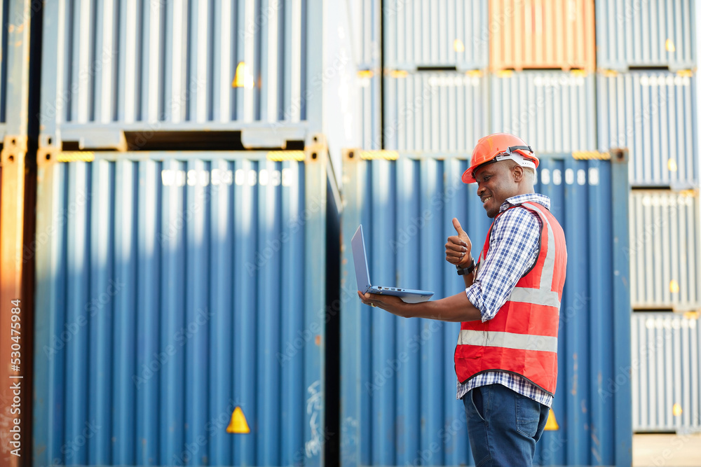 African factory worker or engineer using laptop computer and checking work in containers warehouse storage