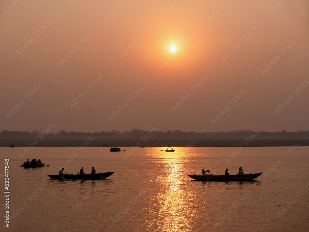 Wooden boats being rowed on the Ganges River at sunrise in Varanasi, India.