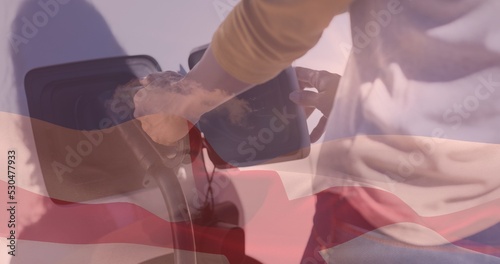 Double exposure of man plugging in charger to electric vehicle at station and english flag