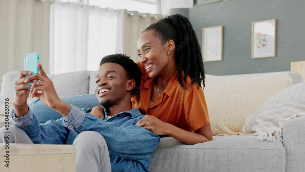 Couple phone selfie, funny communication and relax on sofa in house, comic conversation with social media on smartphone and comedy talking on web. Happy African man and woman taking photo with tech Couple phone selfie, funny communication and relax on sofa in house, comic conversation with social media on smartphone and comedy talking on web. Happy African man and woman taking photo with tech