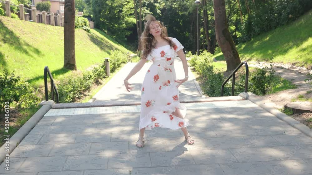 Young female dancer in a summer dress dancing in the park on a sunny summer day