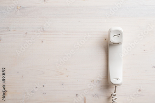 Handset of a white landline phone placed on plain wooden board © Gajus