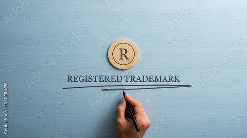 Letter R cut into wooden cut circle and male hand writing a Registered trademark sign under it photo