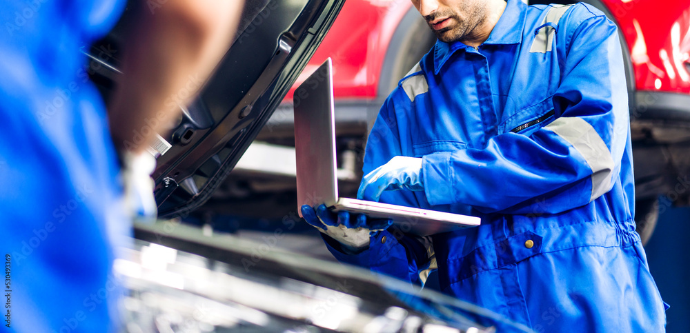 Professional car technician mechanic team in uniform use laptop work fixing vehicle car engine and maintenance repairing checking under the car in auto service. Automobile service garage