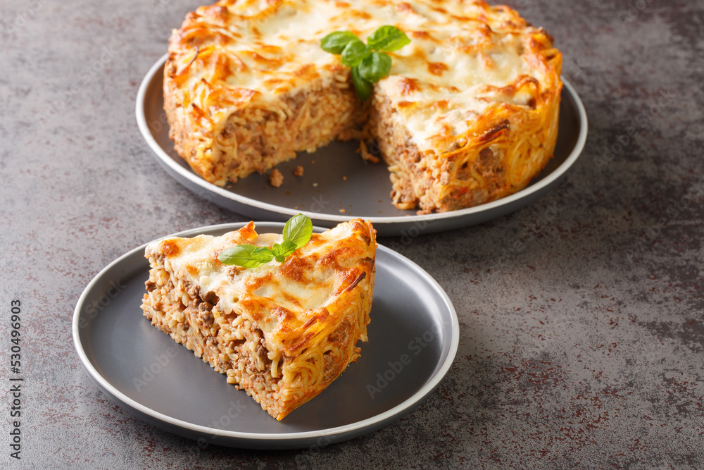 Delicious spaghetti pasta pie with ground beef, tomato sauce and parmesan cheese and mozzarella close-up in a plate on the table. horizontal