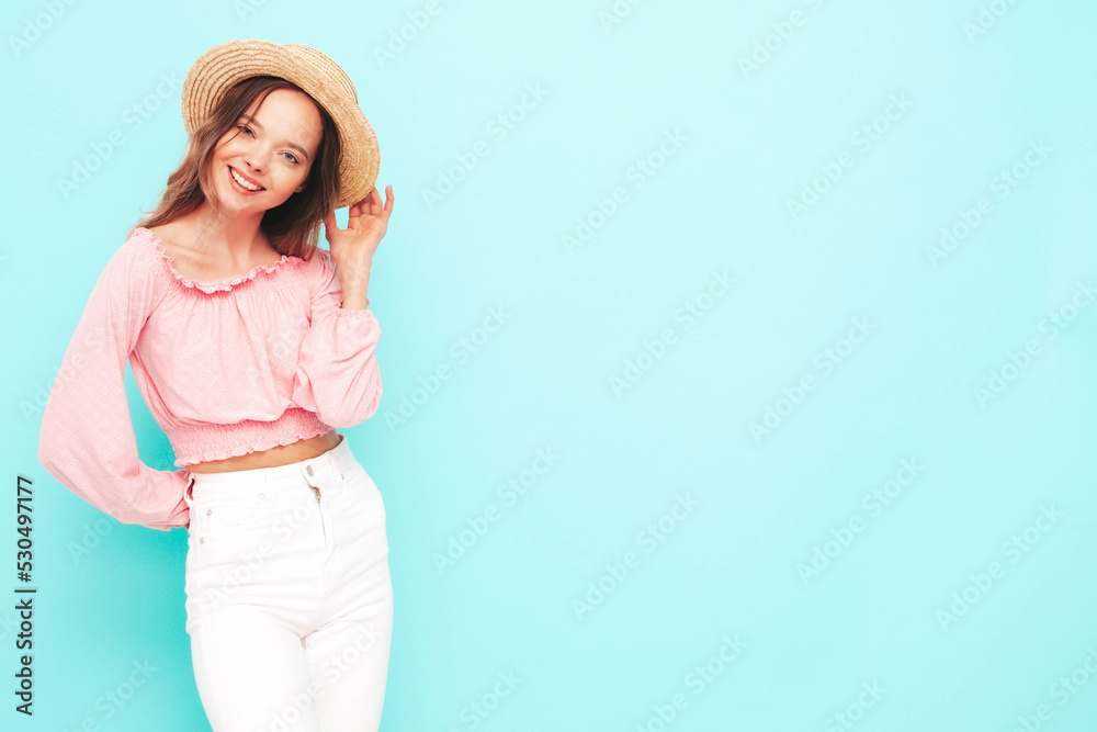 Portrait of young beautiful smiling female in trendy summer  clothes. Sexy carefree woman posing near blue wall in studio. Positive brunette model having fun. Cheerful and happy. In hat