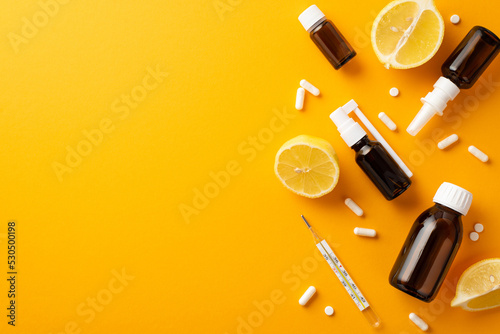 Illness concept. Top view photo of spray and syrup transparent brown bottles pills capsules thermometer and lemon halves on isolated orange background with empty space