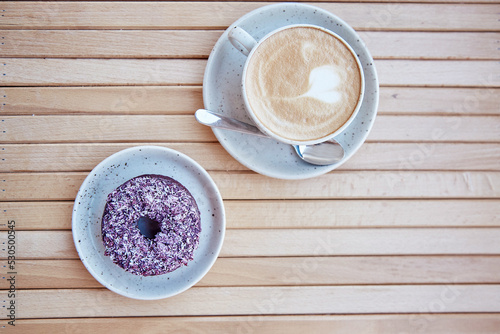 Colorful purple doughnut and cappuccino at the terrace in the cafe. Aesthetic coffee time. Top view, copy space on wooden background