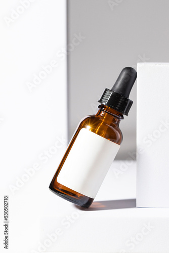Amber glass dropper bottle with black pipette and whita label on white podium.Beauty Cometic product, oil o serum for skin care.