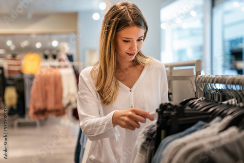 Happy young woman buying new clothes in store. Sale shopping fashion and people concept