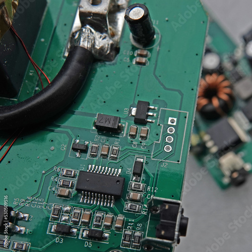 Macro photo of an electronic circuit board of a portable charger with selective focus. A second electronic board with a toroidal inductor is seen blurred beneath