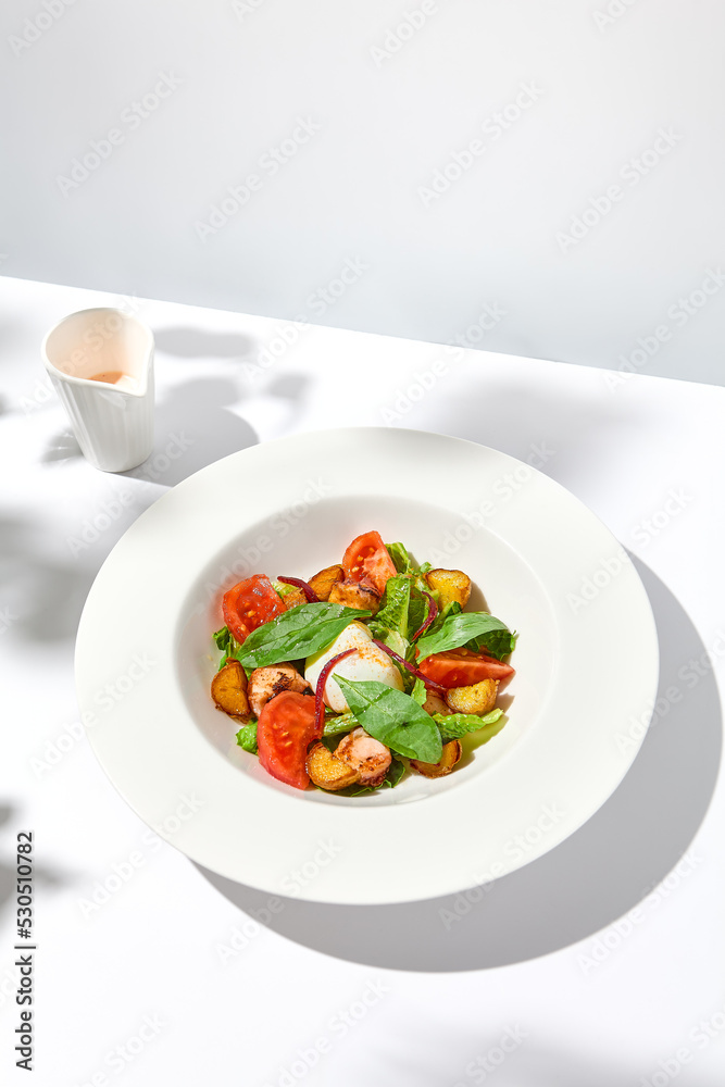 Salad with octopus, baked potatoes and poached egg on white table with hard shadows. Seafood salad with vegetables and potatoes in summer menu restaurant. Octopus and eggs salad in modern style.