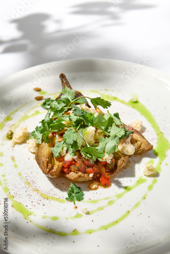 Baked eggplant with cheese on white table with harsh shadows. Aesthetic italian food - baked aubergine on white plate. Stuffed eggplant in minimal style. Stuffed aubergine in vegan menu.