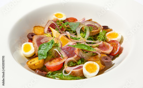 Traditional french salad nicoise with tuna, potatoes, eggs and vegetables on white table with harsh shadows. Tuna salad with quail eggs on white background with shadows of leaves.