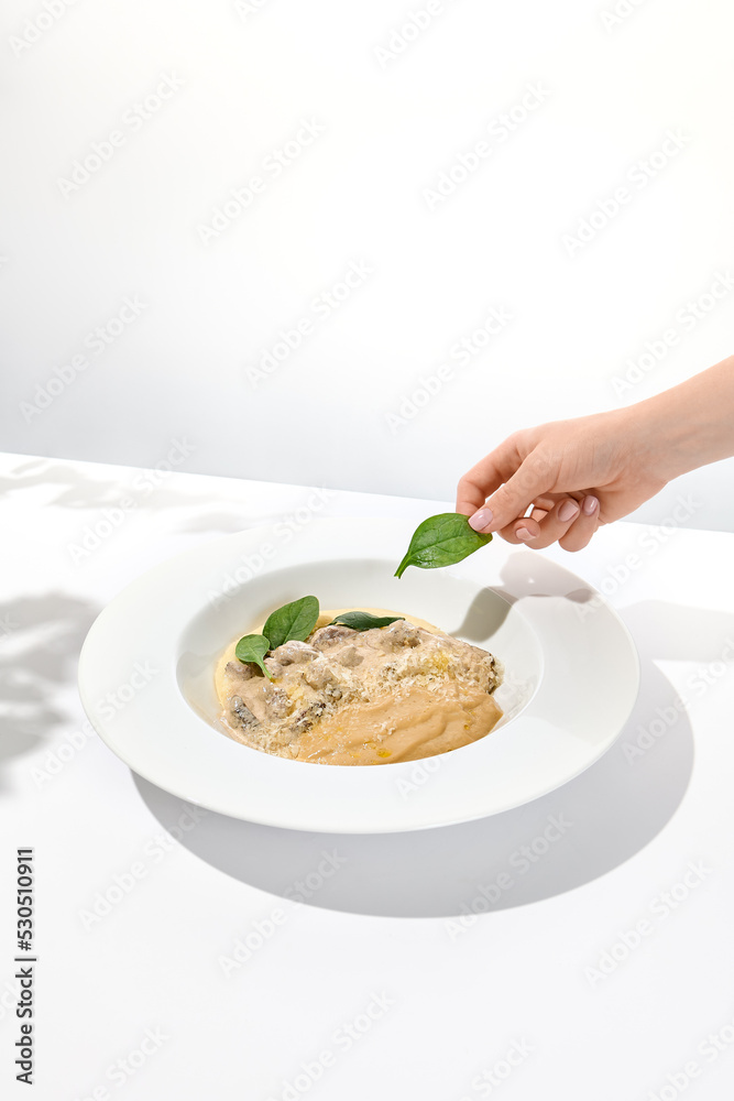 Female hand take spinach leaves over restaurant dish. Person cooking meat dish with spinach holding leaves. Trendy menu concept. Meat dish with young woman hand. The cooking process.