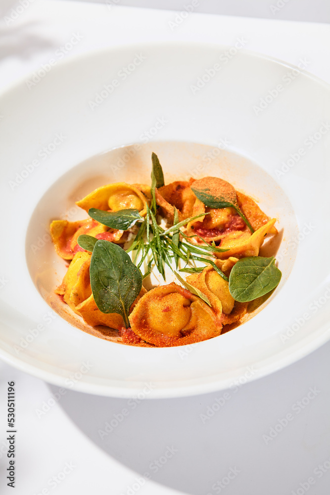 Tradition italian stuffed pasta - tortellini with minced meat. Italian ravioli on white background with harsh shadows. Summer menu italian restaurant. Tortellini with beef and spinach leaves Tradition italian stuffed pasta - tortellini with minced meat. Italian ravioli on white background with harsh shadows. Summer menu italian restaurant. Tortellini with beef and spinach leaves