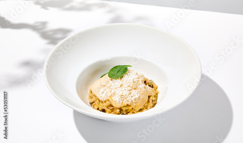 Italian food - mushrooms risotto with creamy espuma on light background. Mushroom risotto with cheese in summer menu Italian risotto with hard shadows from tree leaves. Trendy menu concept