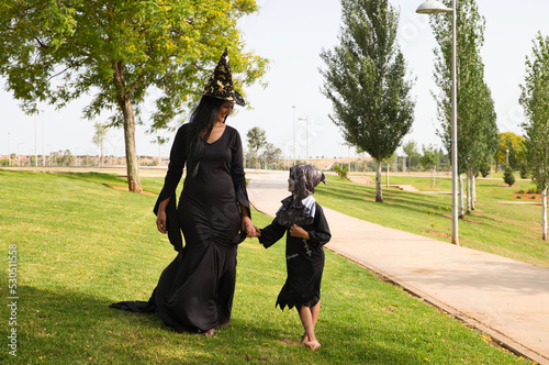 Happy halloween. Child dressed up for halloween party and his mother dressed as a witch walking in the park. Trick or treat.