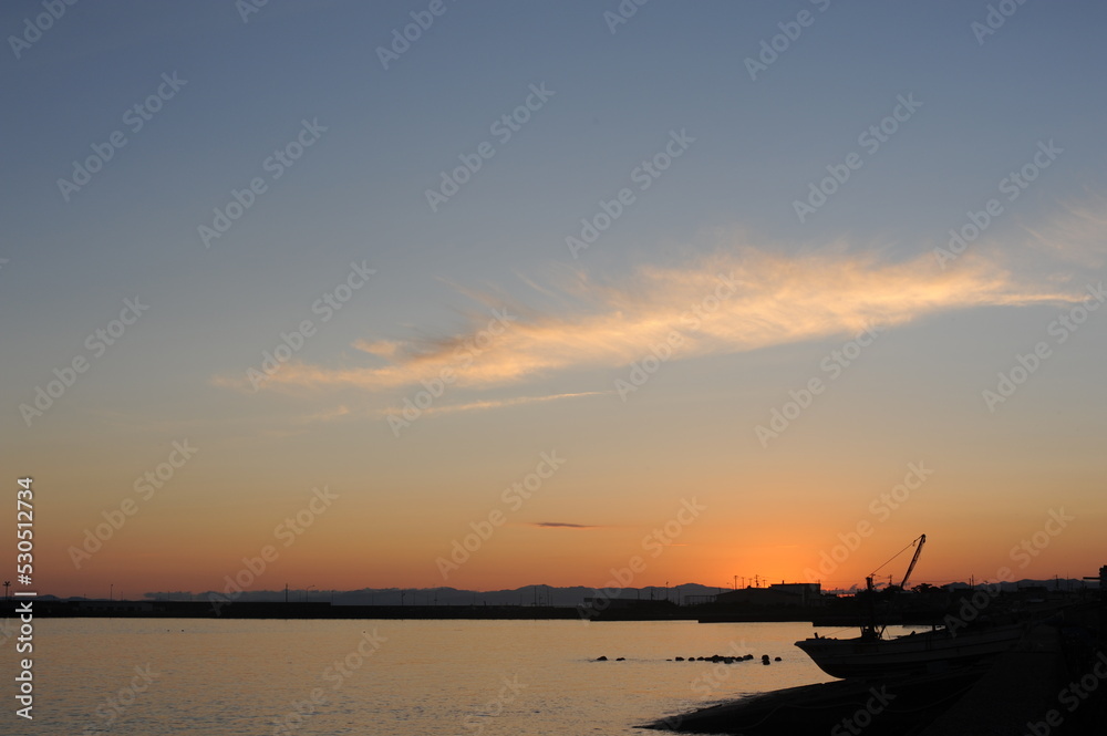 Sunset with a clear sky and sunlight reflexing on the surface of an ocean in the evening at the beach at the sea in fishing town in summer in Japan Sunset with a clear sky and sunlight reflexing on the surface of an ocean in the evening at the beach at the sea in fishing town in summer in Japan