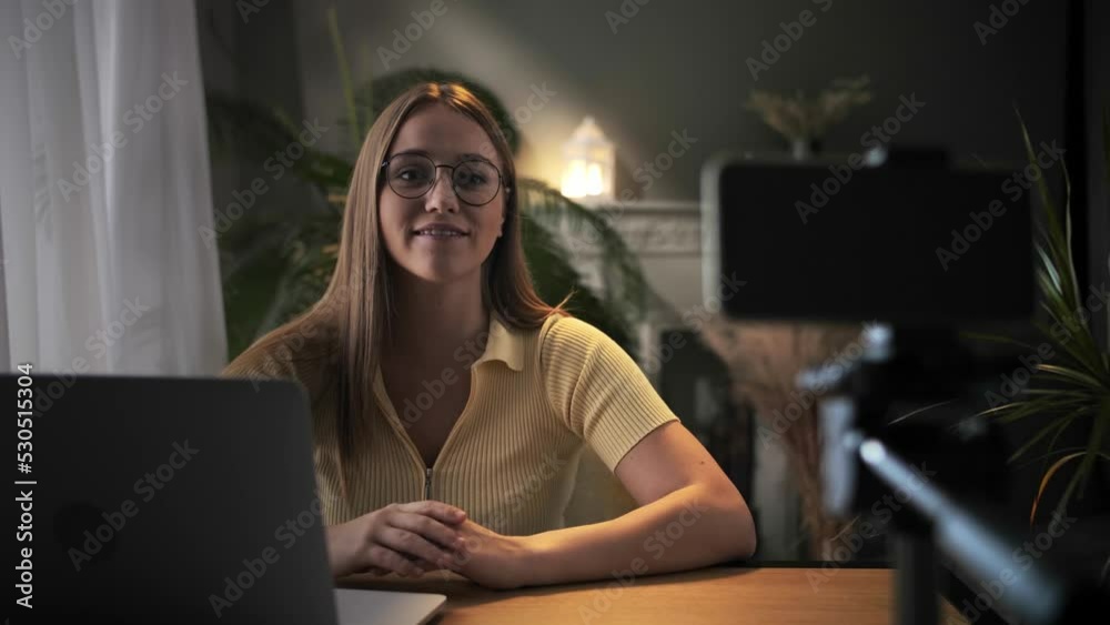 Woman record online lesson using smartphone in home interior.Young blonde hair girl talking head looking at camera cellphone on tripod.Smiling female teacher english class.