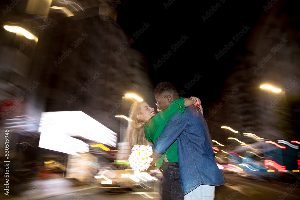 Multiethnic couple embracing in the street at night