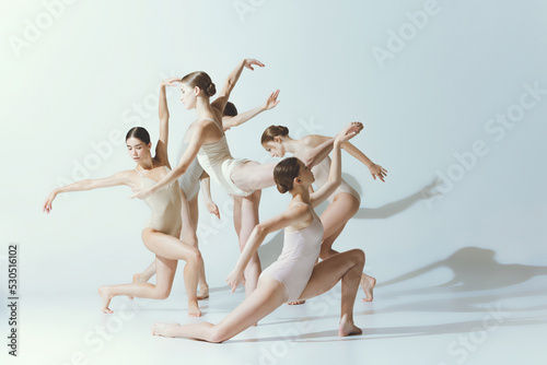 Group of young women, ballerinas dancing, performing isolated over grey studio background. Attraction of choreography
