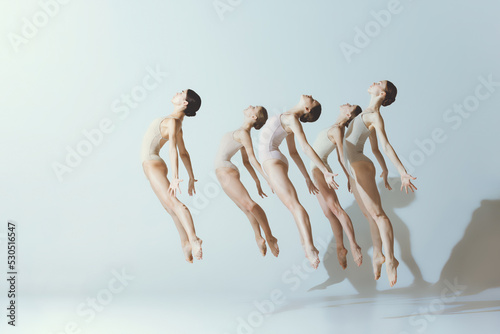 Group of young girls, ballet dancers performing, posing isolated over grey studio background. Jump of freedom