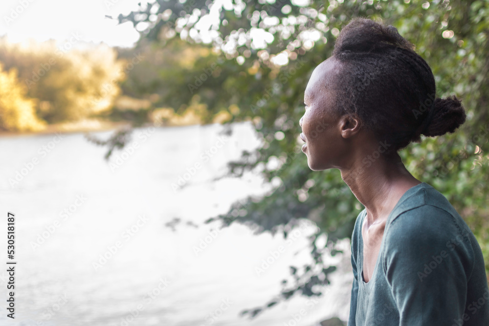 Portrait of afro american young black woman looking at the horizon in in a relaxing, peaceful environment in nature. Female on the river bank. Copy space. Positive expression. Portrait of afro american young black woman looking at the horizon in in a relaxing, peaceful environment in nature. Female on the river bank. Copy space. Positive expression.