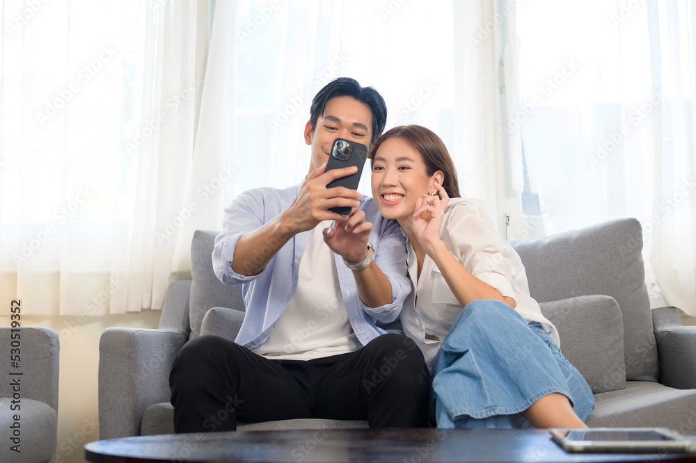 Young smiling asian couple holding smartphone and making video call at home