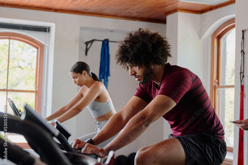 Obraz premium Young middle eastern man and biracial woman cycling on exercise bike at the gym