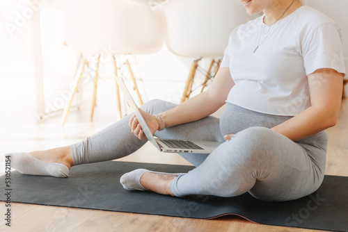 Fototapeta Naklejka Na Ścianę i Meble -  Young pregnant blonde woman practicing online yoga at home with laptop background white kitchen