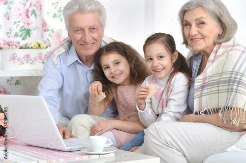 Grandfather and grandmother with children are sitting with a laptop