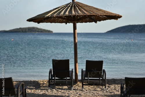 Fototapeta Naklejka Na Ścianę i Meble -  Beautiful shot of chairs and an umbrella on a calm beach in Sibenik, Croatia