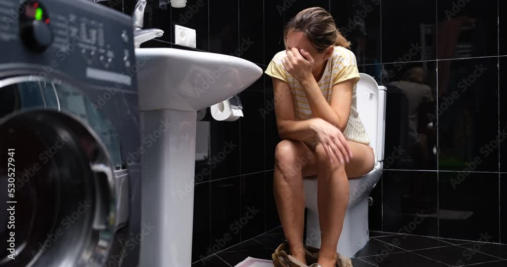 Young woman is crying in pain while sitting on toilet Young woman is crying in pain while sitting on toilet