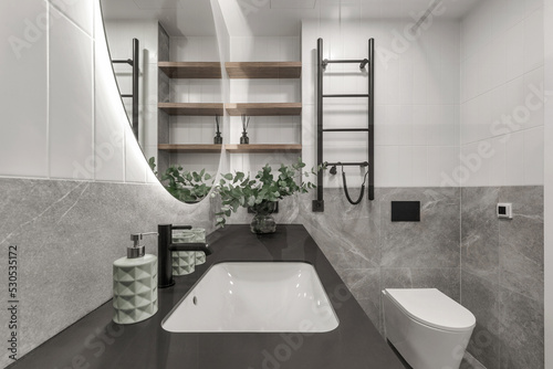 Modern minimalistic bathroom interior design with grey stone tiles  black furniture  eucalyptus in glass vase  round mirror.  Aesthetic simple interior design concept.