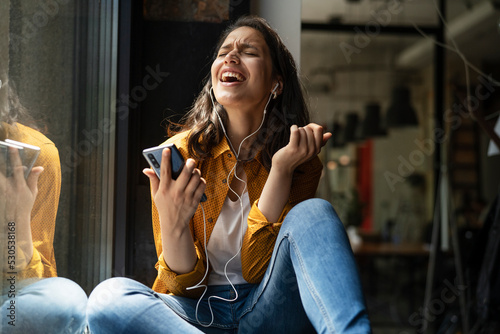 Young woman sitting and listening the music. Portrait of happy woman listening music with earphones while singing song..