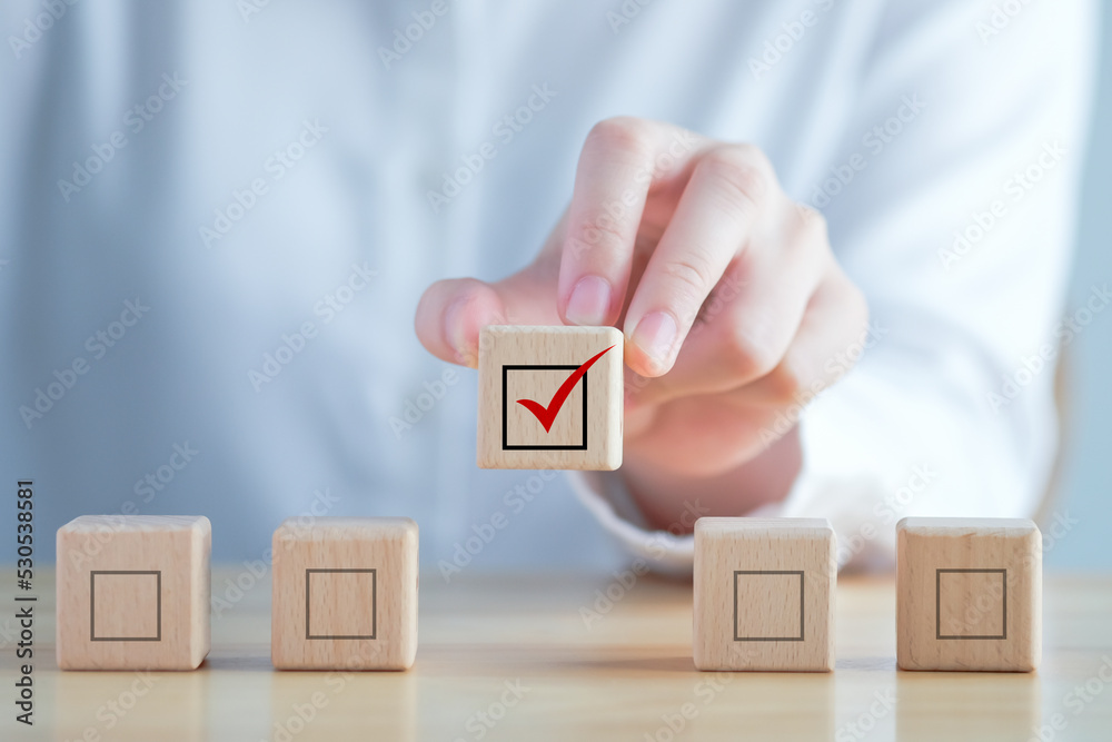 Elections and Voting, Vote, to do list, checklist, Task list, Survey and assessment concept. Hand holding check mark on wooden block and blank check box on wooden cubes. Elections and Voting, Vote, to do list, checklist, Task list, Survey and assessment concept. Hand holding check mark on wooden block and blank check box on wooden cubes.