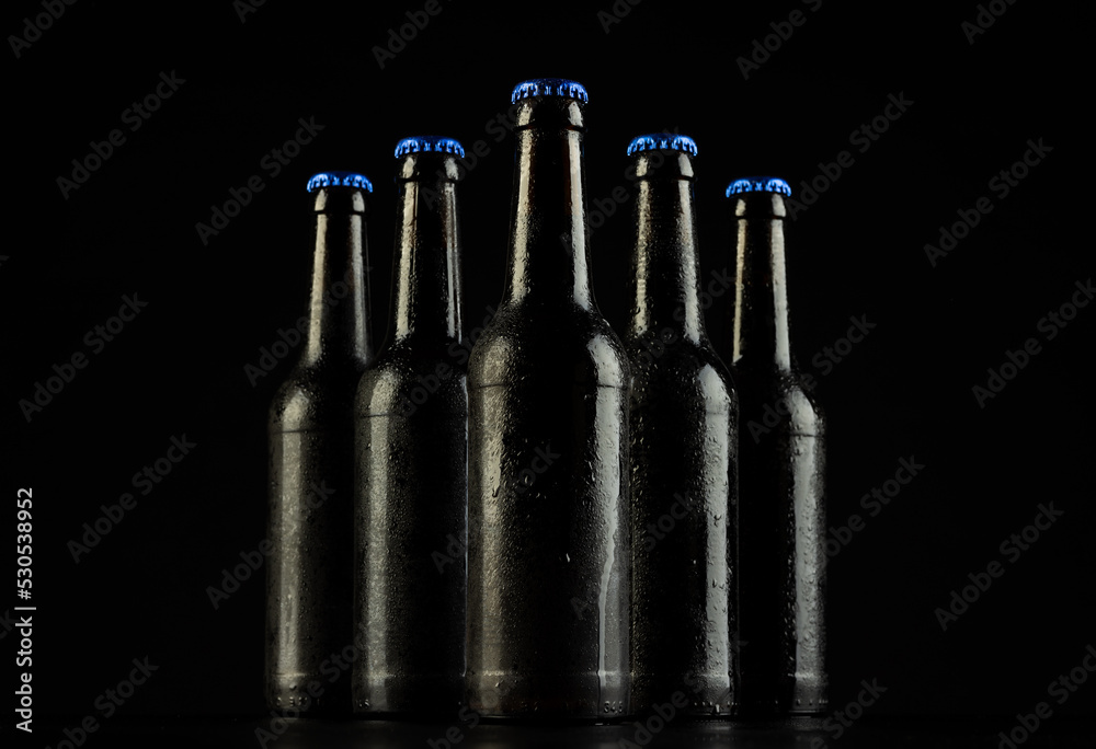 Image of five beer bottles with blue crown caps, with copy space on black background - obrazy, fototapety, plakaty 