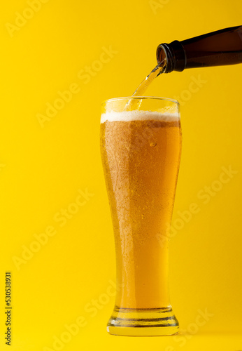 Image of beer bottle pouring into pint glass of lager beer, with copy space on yellow background
