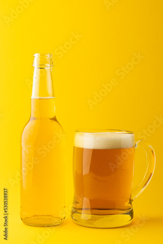 Image of full clear glass bottle and glass tankard of lager beer, with copy space on yellow