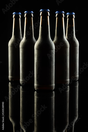 Vertical image of five dark glass bottles of lager beer with blue caps on black, with copy space