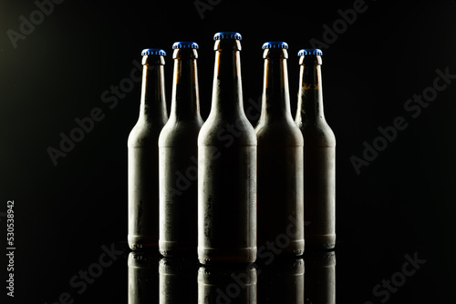 Horizontal image of five dark glass bottles of lager beer with blue crown caps on black background