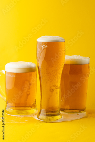Image of three different full pint glasses of lager beer, with copy space on yellow background