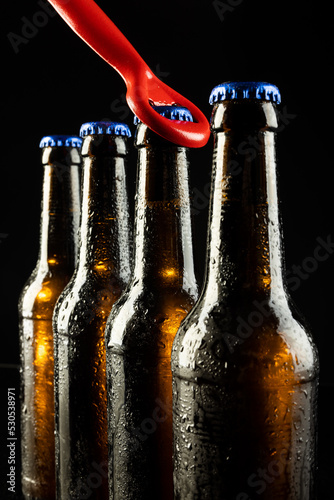 Image of red bottle opener and four beer bottles with blue crown caps, with copy space on black