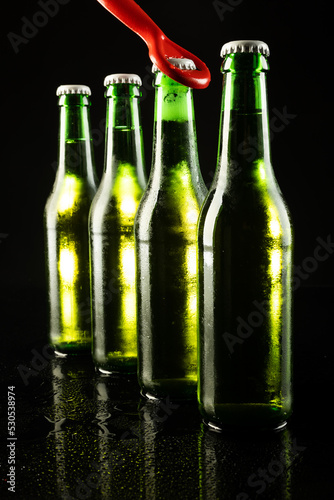 Image of red bottle opener and four green beer bottles with crown caps, with copy space on black