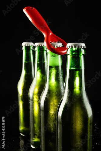 Image of red bottle opener and four green beer bottles with crown caps, with copy space on black