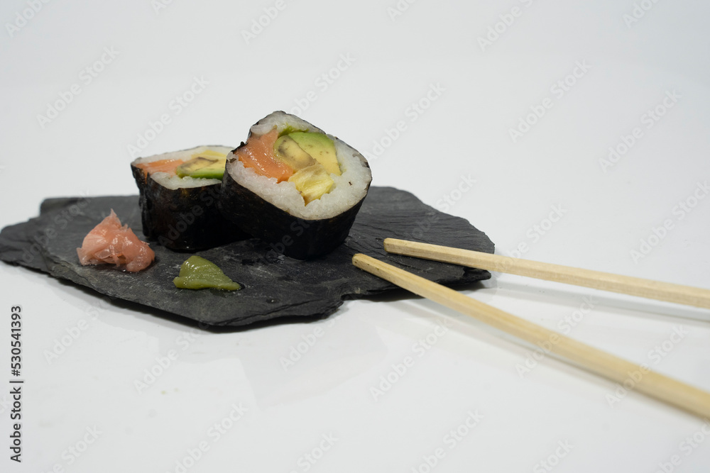 two pieces of sushi in a blackboard plate with chopstick, ginger and wasabi two pieces of sushi in a blackboard plate with chopstick, ginger and wasabi