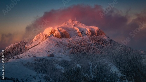 Scenic view of the snowy Toaca peak in Ceahlau Mountain against dusk sky, Romania photo