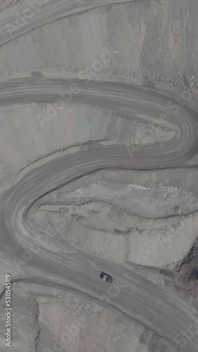 Vertical drone shot of a dump truck transporting coal over hairpin gravel dirt road inside a massive open mine in China
 photo