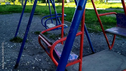 old and empty swings move from side to side on the playground during the daytime.